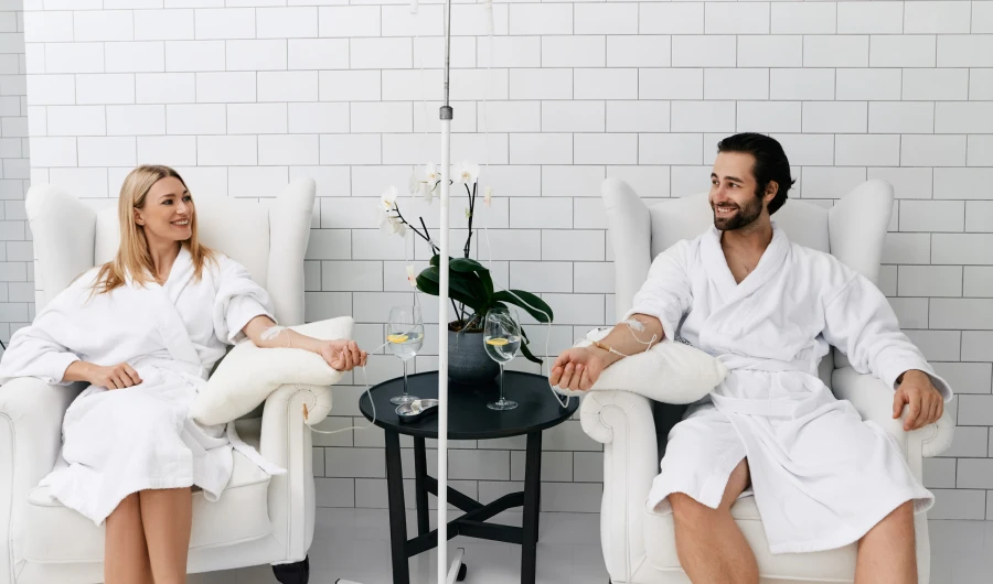 a person and person in white robes sitting in chairs with drinks in a room