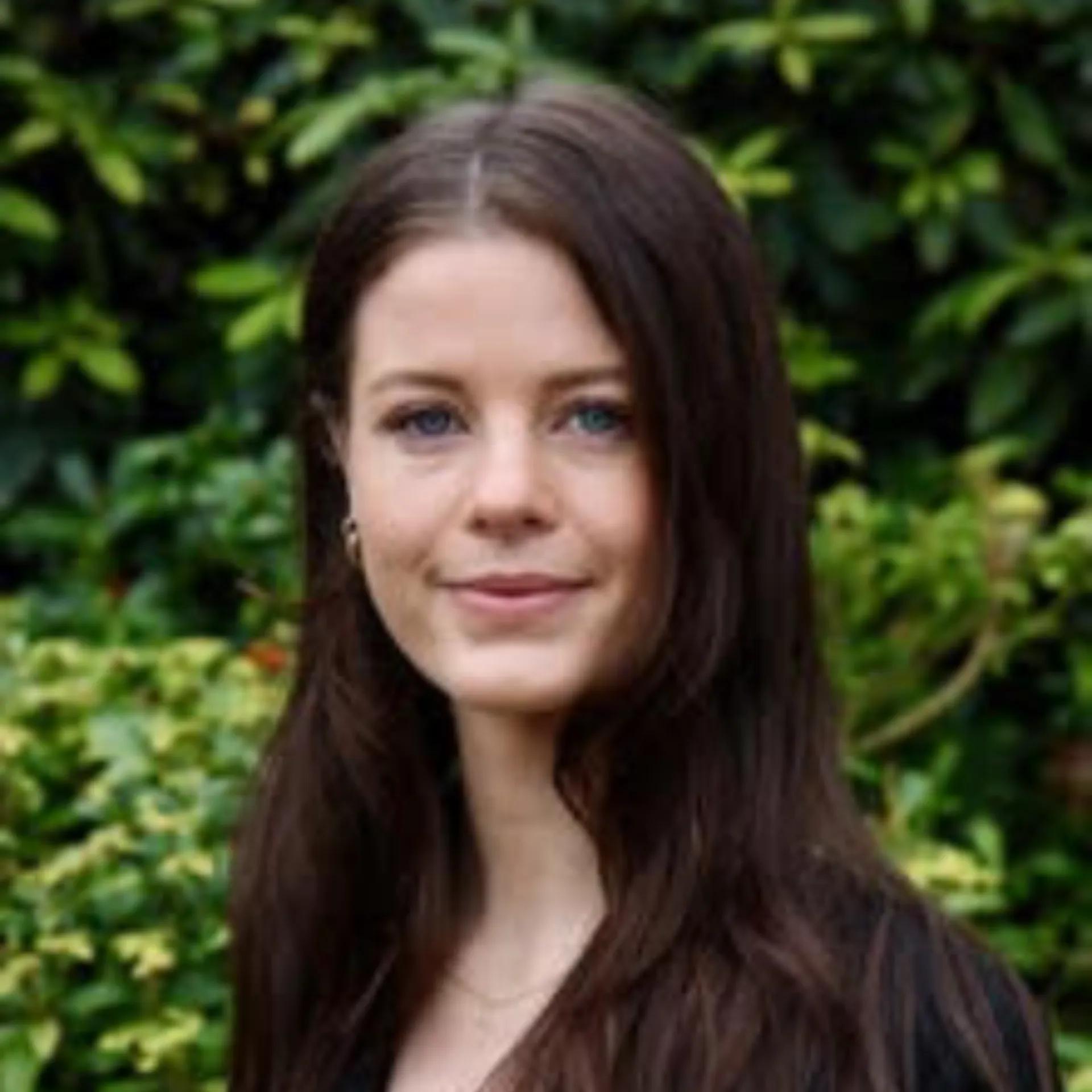 A person with long brown hair and a black top stands outdoors in front of green foliage, looking at the camera, perhaps reflecting on their thoughts about ZIPDRIP.