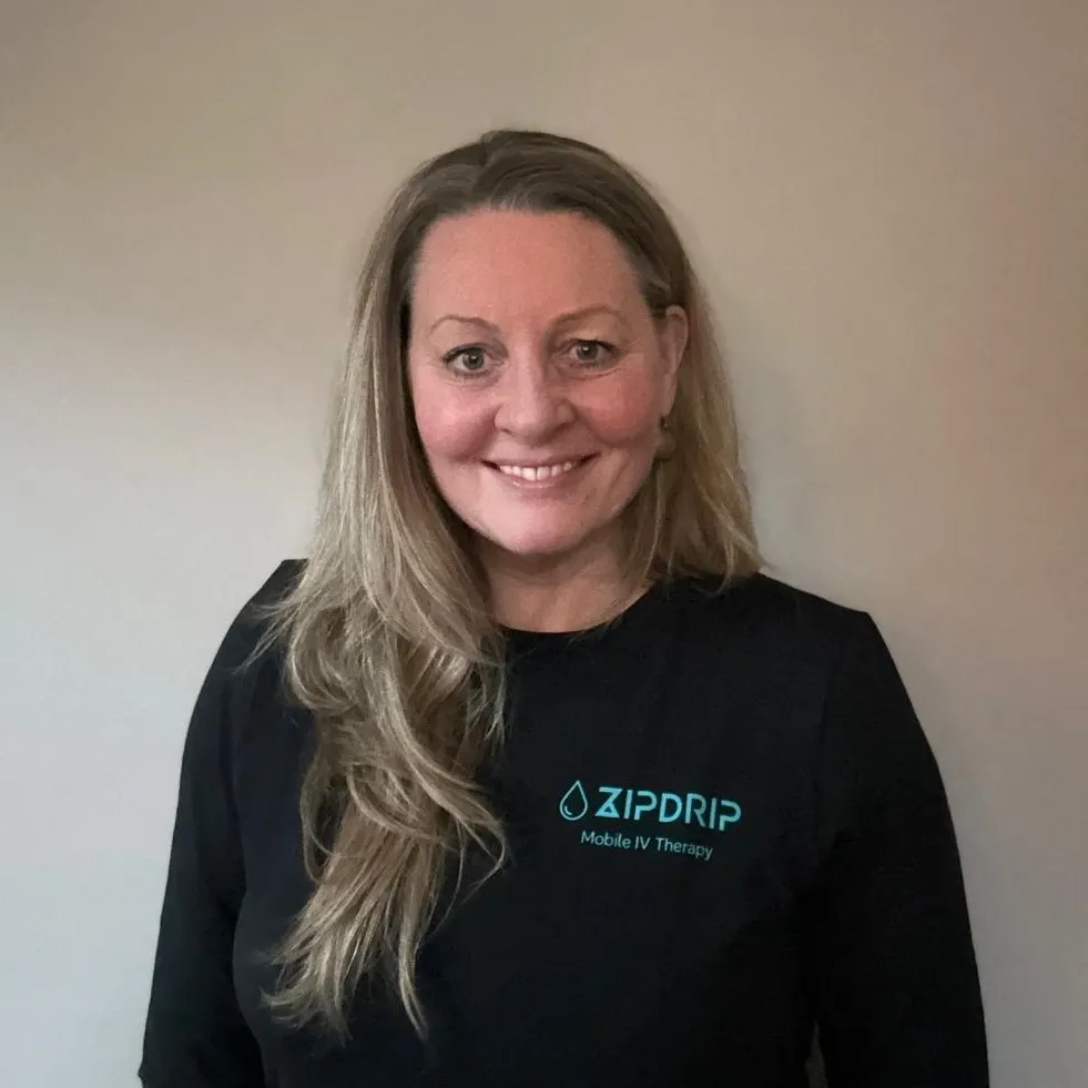 Smiling person in a black shirt with a "ZIPDRIP Mobile IV Therapy" logo, standing against a plain background.