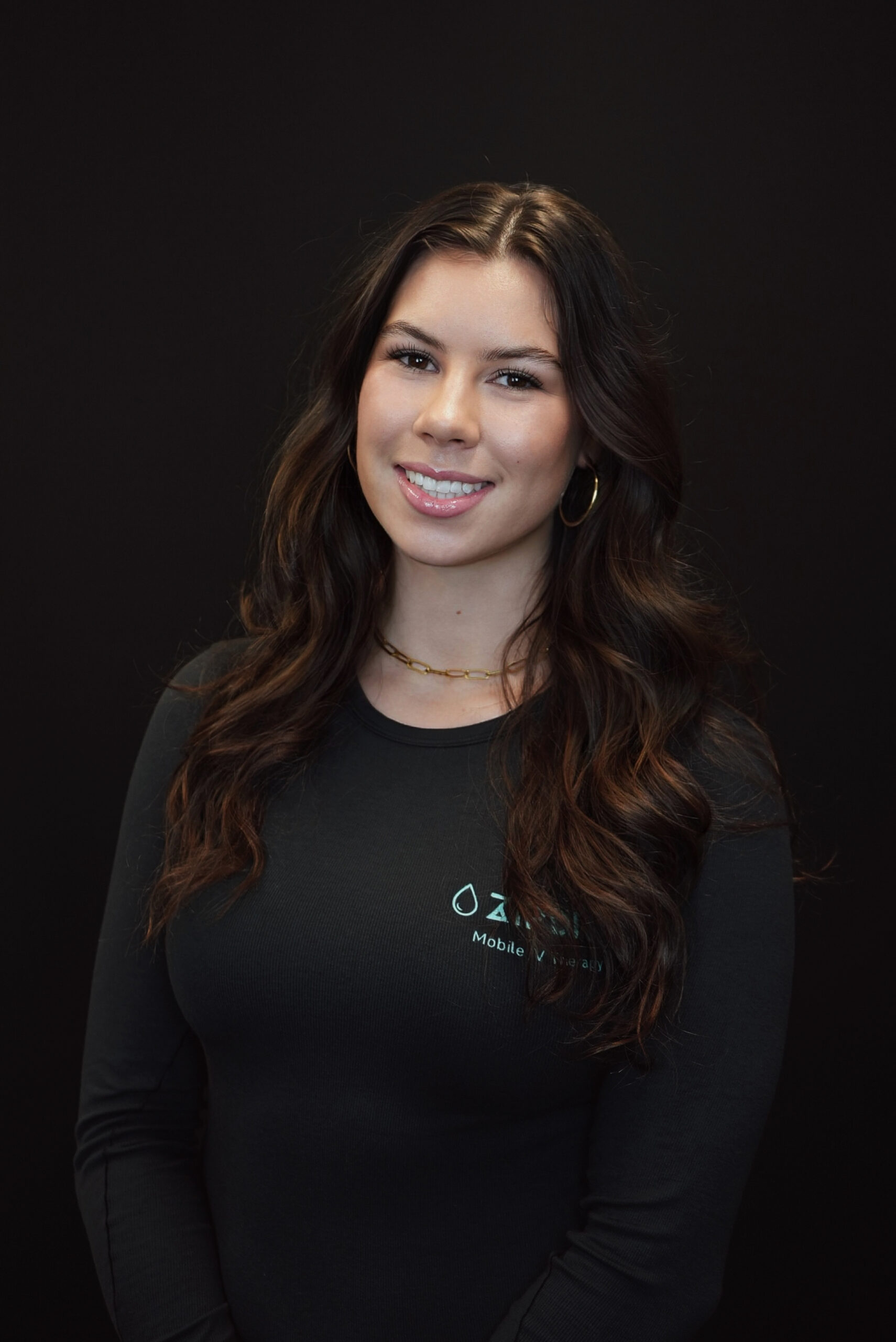 A woman with long dark hair, wearing a black top with a small About ZIPDRIP logo, stands smiling against a plain black background.
