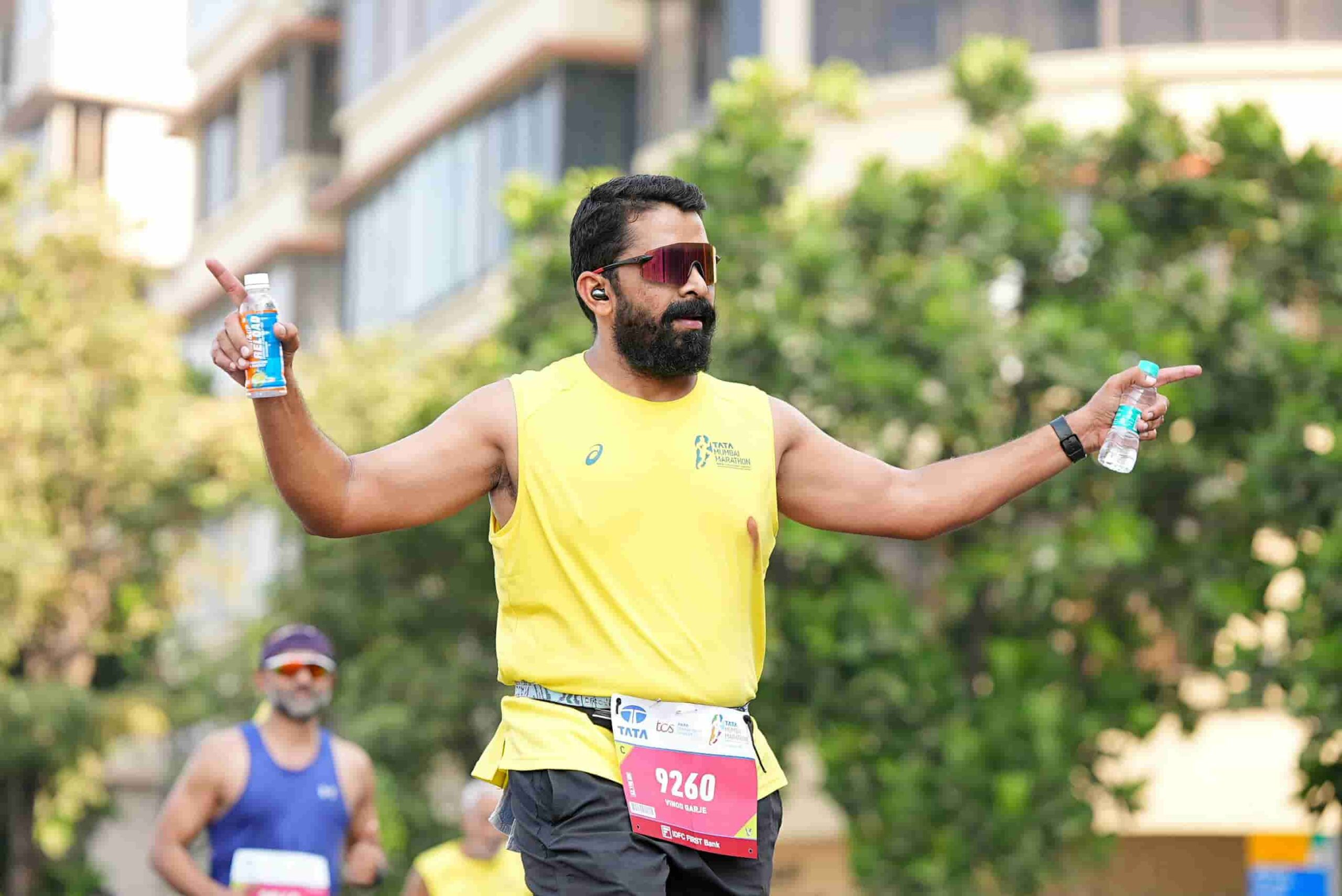 A man in a yellow tank top running a marathon, holding a water bottle and an energy drink with race bib 9260, gestures with both arms—raising the question: How Often Should Vancouver Runners Get IV Hydration Sessions?.